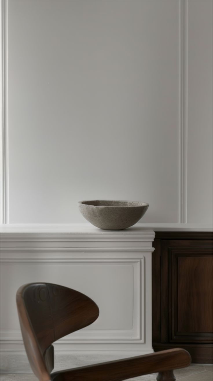 A minimalist interior scene featuring a warm-toned chair beside white high shelving, styled with a soft grey pastel bowl, creating a calm and neutral aesthetic suitable for a zodiac wall art collection cover image.